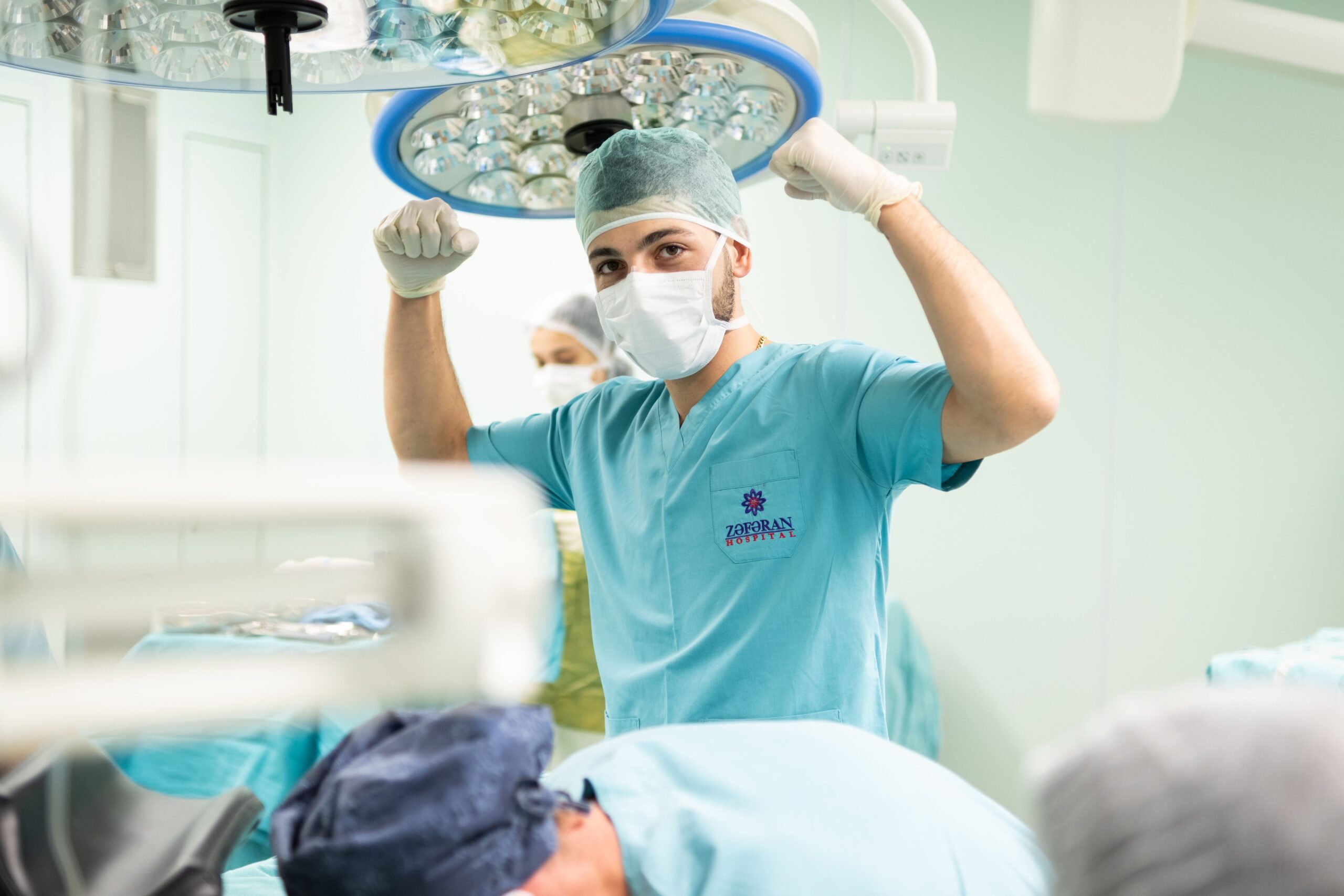 A surgeon in scrubs celebrates after a successful surgery in an operating room.